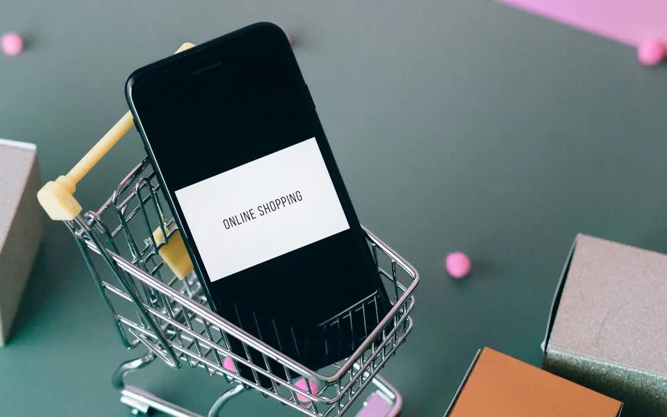A smartphone in a small shopping trolley beside packaging