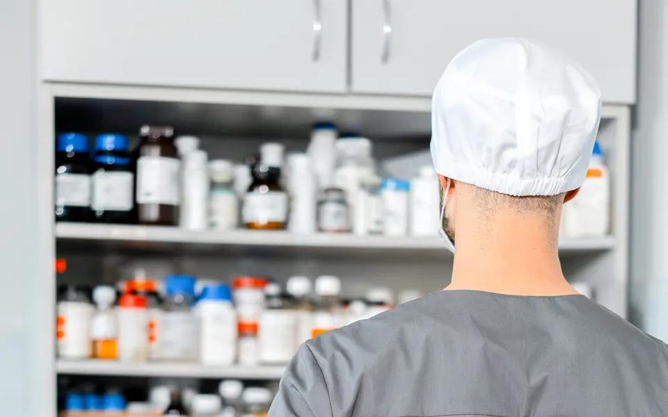 A pharmacist standing beside stocked medicine shelves